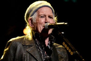 Keith Richards performs onstage during the Sixth Annual LOVE ROCKS NYC Benefit Concert For God's Love We Deliver at Beacon Theatre wearing a beanie and leather jacket standing in front of a microphone.