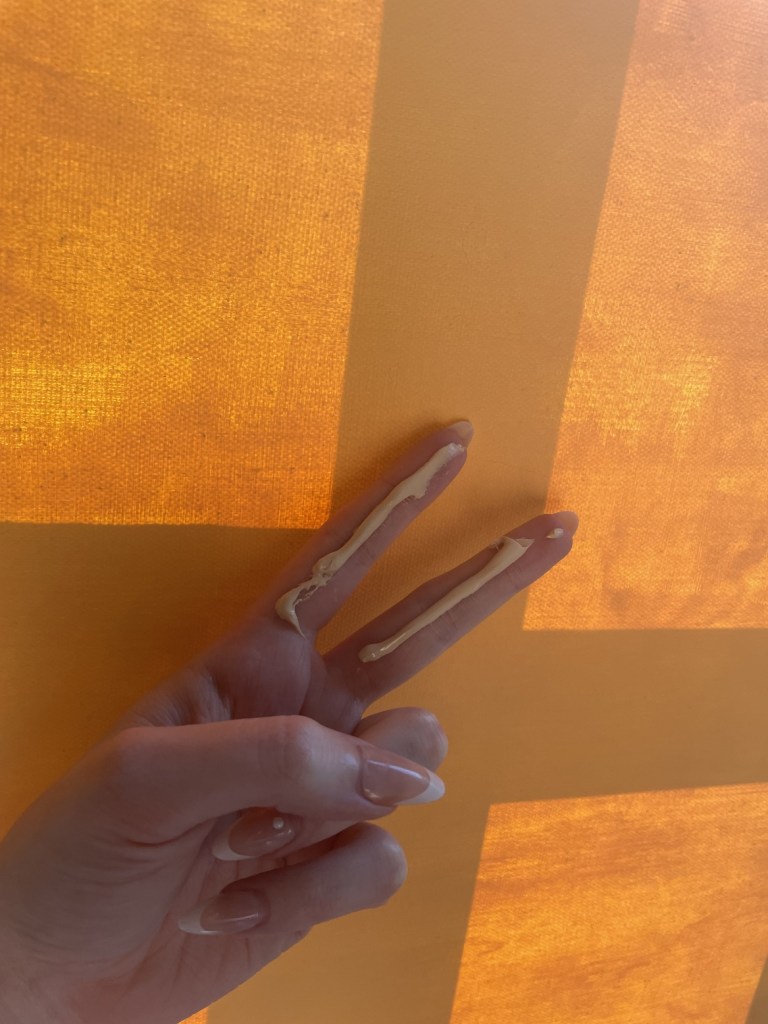 2 fingers length of sunscreen, posed in front of an orange background 